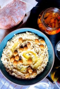 Classic hummus garnished with chickpeas and olive oil, in a blue bowl. A basket of pita bread and a jar with red roasted peppers in oil, above. Vegan, glutenfree, easy
