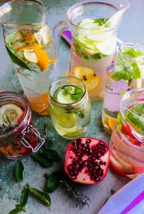 Glass jars and bottles with colourful fruits and herbs in water for naturally flavoured water made at home. Strawberries, cucumber, orange and lemon in combination with basil, mint and rosemary