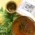 A brass bowl with brownish liquid neem flower raw mango rasam, tempered with neem flowers fried in ghee, mustard, cumin seeds, curry leaves and red pieces of tomato visible on top. A traditional tamil cookery book with a white cover to the left with a black and white image of the author. A little brass bowl with fried neem flowers on the left with a bunch of neem (margosa) leaves and flowers