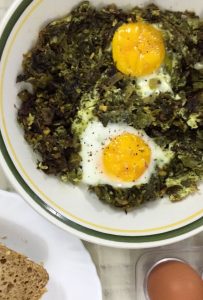 Green Kale Shakshuka with the cooked kale spread on a white plate with a green and yellow edging. Two eggs with their yolks resting on the kale