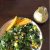 Marinated Kale Mango Salad served on a white plate with slices of yellow ripe mango heaped to the left of the plate. Cubes of mango seen among the green kale and salad greens on the plate. A small jar of creamy tahini citrus dressing on the top right, all on a dark brown background