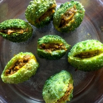 Process shot: Small bitter gourds stuffed with mustard coloured raw mango and onion filling, ready to be cooked