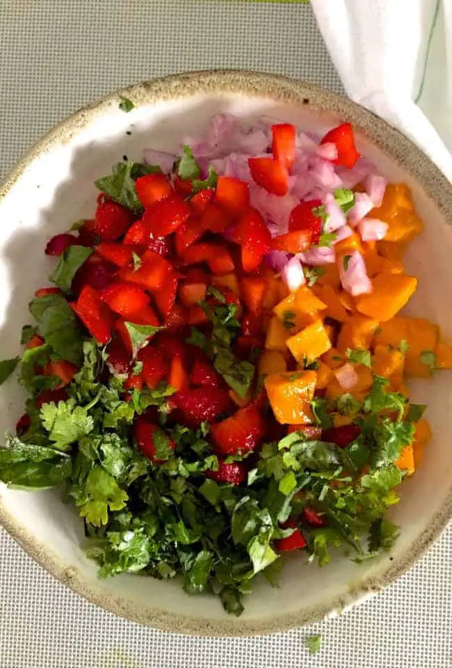 Sliced ingredients for the salsa, before being tossed together - orangey yellow mango, red strawberries, green basila and cilantro and pink onion