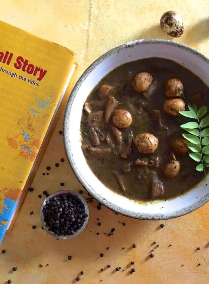 Kaada Muttai Milagu Kuzhambu: A white bowl with quail eggs in a pepper tamarind gravy. A yellow covered book with the name 'The Tamil Story' in Red, on the left and a bowl of pepper and scattered peppercorns in the foreground. A few speckled quail eggs in the background