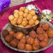 A plate of vella seedai from Store bought flour, with a bowl of smaller uppu seedai all on a pink silk fabric with a purple flower in the background and small silver lamps just behind the plate