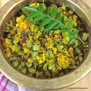 Green and yellow dry curry in a brass bowl with a sprig of curry leaves on top, a pink and white napkin seen to the bottom left. Kothavarangai Paruppu Usili, tender cluster beans sliced thin and cooked with a paste of cooked lentils, tempered with mustard and chili. 