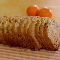 Slices of pale golden orange honey pistachio cake, on a striped board, with 2 bright oranges in the background, all on a pale yellow backdrop