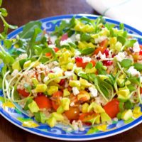 Bright coloured barley salad with tomato, avocado, microgreens, on a plate with blue and yellow scrolled design. A white napkin with green stripes at top right corner