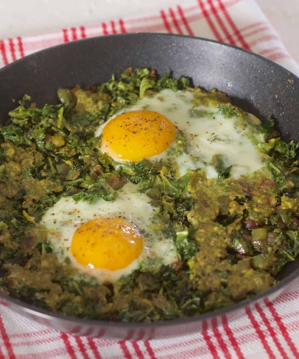 Two open faced eggs on a sauce of sauteed kale and onion with a parsley pesto