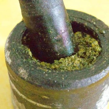 Easy Basil Pesto made instone mortar and pestle, with some of the mustardy green pesto showing at the top of the mortar. On a yellow background