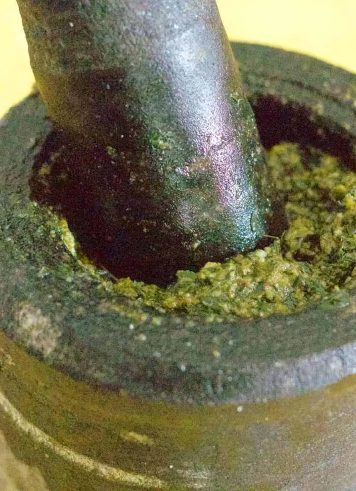 Easy Basil Pesto made instone mortar and pestle, with some of the mustardy green pesto showing at the top of the mortar. On a yellow background