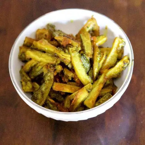 Thin strips of yellow green bitter gourd fry/ karela/ pahakkai in a white bowl on a brown wooden background