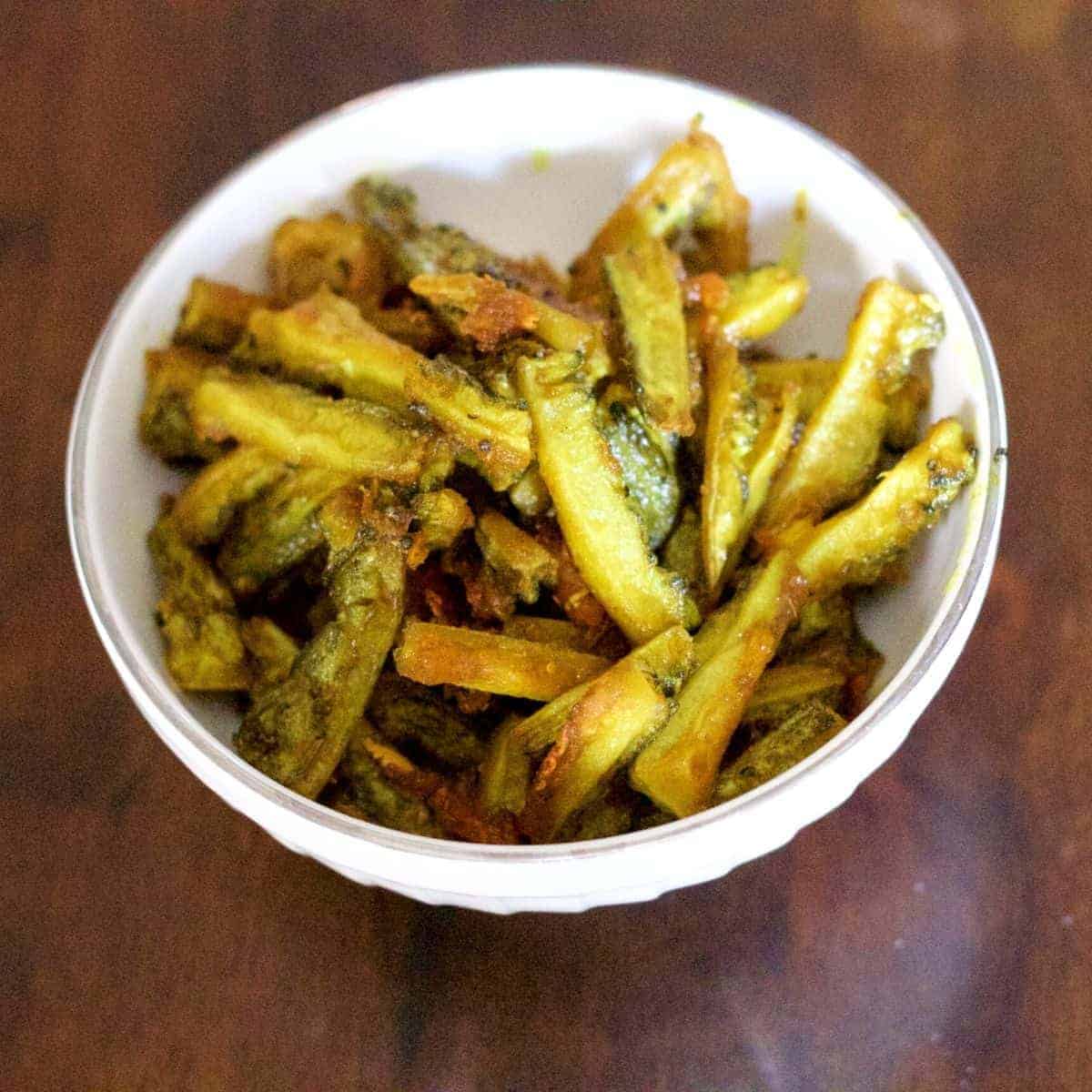 Thin strips of yellow green bitter gourd fry/ karela/ pahakkai in a white bowl on a brown wooden background