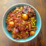 A blue bowl with orange red Odia Cabbage Potato Peas Curry, on pale brown background