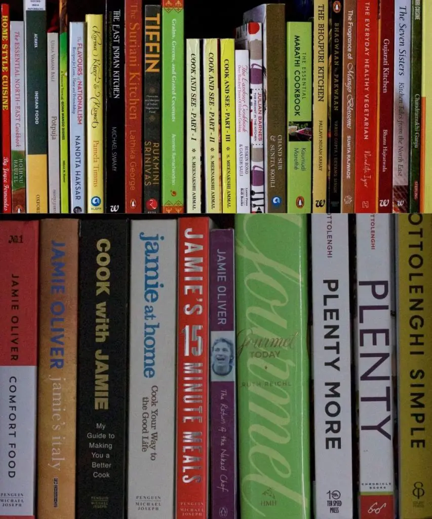 Rows of different coloured cookbooks on two shelves for cooking from cookbooks