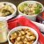 White bowl with brown spiced cooked double beans with a jar of beige spice mix to the left, two bowls with cooked beans of different flavours at the back and red and white napkin to the left