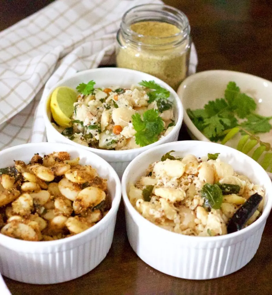 3 white bowls each filled with a different flavour of mochai sundal/ cooked double beans. Plate with green cilantro and curry leaves on one side, slice of lemon in one bowl and beige spice mix in a glass jar at the back. Beige and white checked napkin at the left