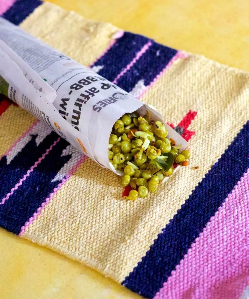 Thenga Manga Pattani Sundal_Cooked green peas with shavings of coconut and raw mango spilling from a newspaper roll onto a cream and pink striped mat, on a yellow background