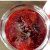 Glass jar full of ruby red jam, on a brown wooden background with a pink and white napkin on the side.