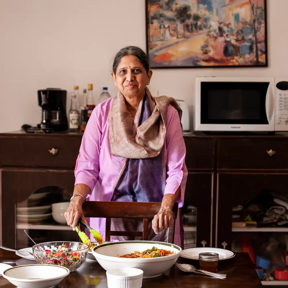 Image of the author serving food. Penne pasta in an orange coloured sauce, green basil leaves in a white pasta dish. A glass bowl with a colourful orange, brown, green red salad. Ohter plates and dishes on the table