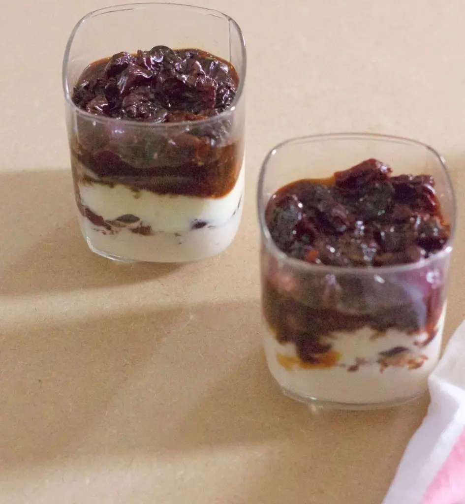 Two glasses with layers of yogurt and cherries, topped by cherry compote. On a beige background Pink and white napkin to the right