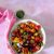 Cherry tomatoes, red, black, green, yellow all sliced into a white bowl. Garnish of colourful flowers yellow, white, purple, orange and basil leaves. On a pale pink background. Bowl with green basil dressing to the back. Pink napkin with white thread to the left
