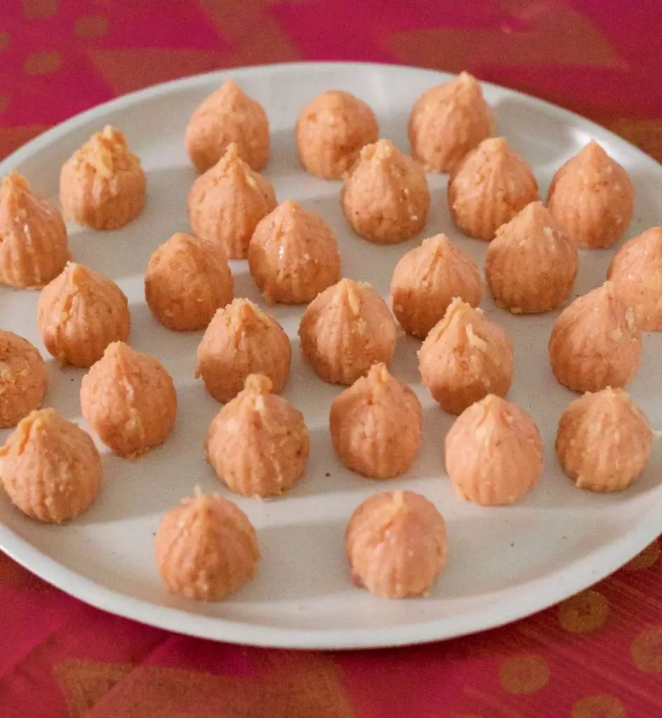 Little pale pink round modaks with pointed tops, all on a white plate on a pink and gold fabric background