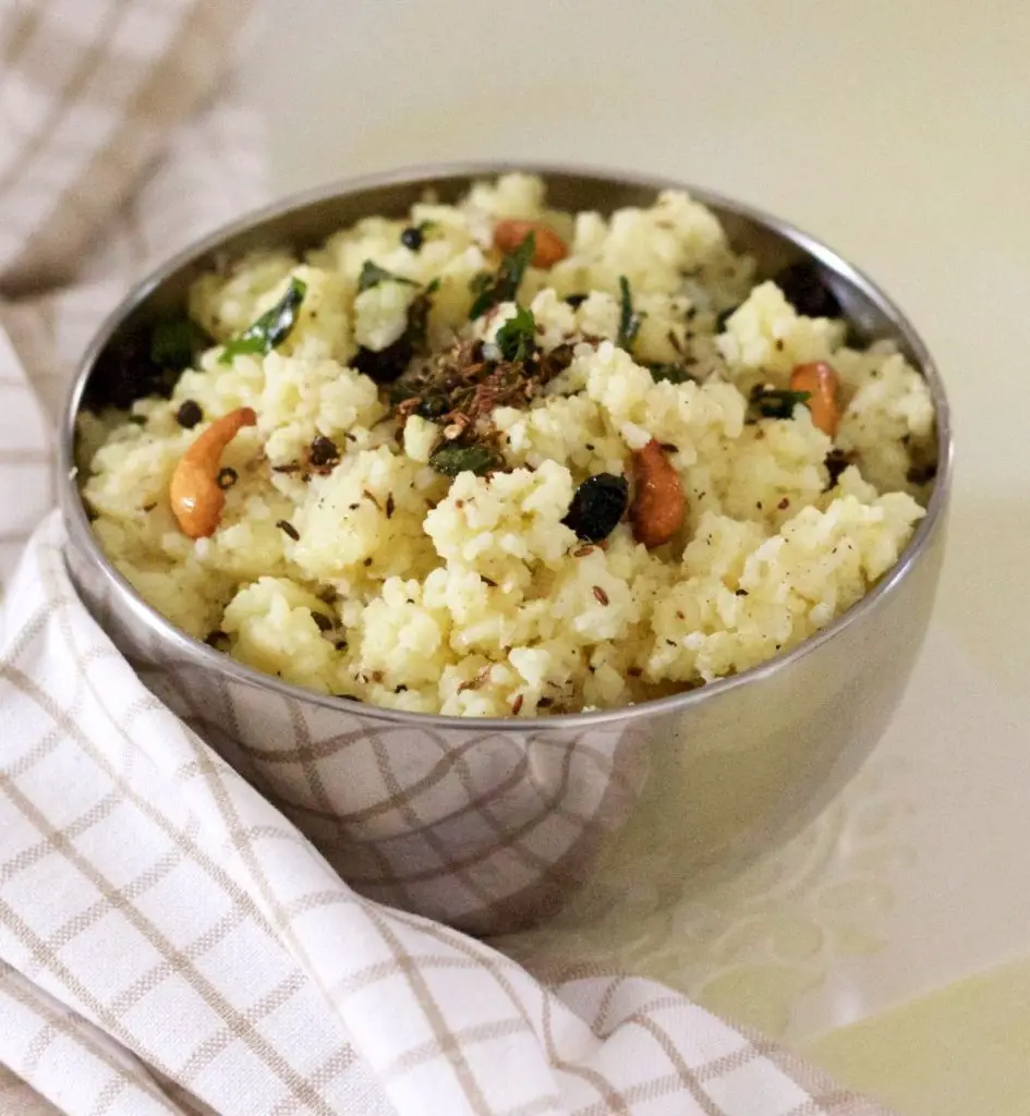 Steel bowl filled with ven pongal a rice and lentil dish tempered with cumin and pepper and garnished with cashew and raisins