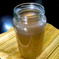 Glass jar with pale brown clear vegetable stock, on a yellow striped mat with a dark blue black background